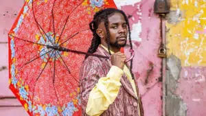 Person holding a red floral umbrella and wearing a patterned suit stands against a graffiti-covered wall, capturing the raw essence of Unfiltered Africa while looking directly at the camera.