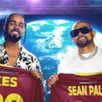 Two men hold up shirts with their names "KES" and "SEAN PAUL" printed on the back, standing in front of an Earth backdrop. Both are smiling, and there is a stage light behind them. This visual almost feels like a case study in camaraderie and showmanship.