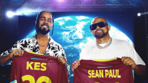 Two men hold up shirts with their names "KES" and "SEAN PAUL" printed on the back, standing in front of an Earth backdrop. Both are smiling, and there is a stage light behind them. This visual almost feels like a case study in camaraderie and showmanship.