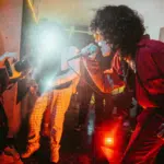 A performer in red sings passionately into a microphone, while photographers capture the moment amidst vivid stage lighting in a crowded room, creating an unforgettable scene ripe for advertising.