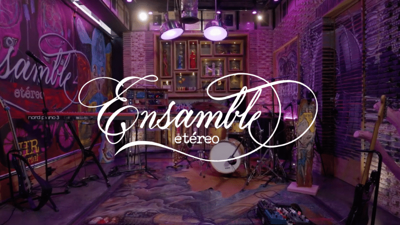 A colorful, artistic music studio with instruments set up, including drums, guitars, and keyboards. The sign "Ensamble Etéreo" is prominently displayed in elegant cursive script, inviting musicians to create ethereal ensembles.