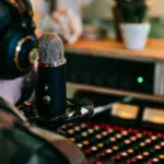 A person wearing TIDAL-branded headphones and a beanie speaks into a microphone in a recording studio, with a sound mixer in the background.