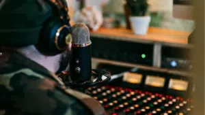 A person wearing TIDAL-branded headphones and a beanie speaks into a microphone in a recording studio, with a sound mixer in the background.