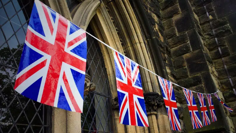 Bunting with multiple Union Jack flags strung along the exterior of a stone building with arched windows.