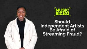 A person in a white jacket stands against a dark background with text: "MUSIC BIZ 101: Should Independent Artists Be Afraid of Streaming Fraud?