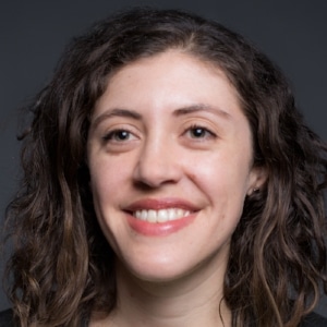 A woman with long curly hair smiles against a dark background.