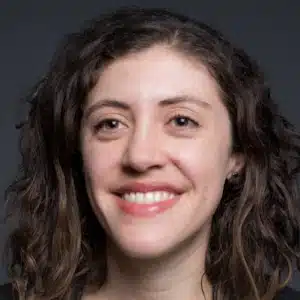 A woman with long curly hair smiles against a dark background.