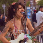 A woman plays the electric guitar and sings outdoors, surrounded by people, creating a vibrant atmosphere fueled by Cosynd's energy.