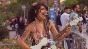 A woman plays the electric guitar and sings outdoors, surrounded by people, creating a vibrant atmosphere fueled by Cosynd's energy.