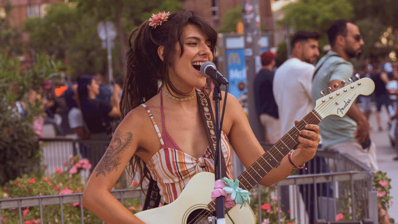 A woman plays the electric guitar and sings outdoors, surrounded by people, creating a vibrant atmosphere fueled by Cosynd's energy.