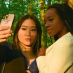 In a sunlit forest, two individuals pose for an elegant selfie, capturing their formal attire's sleek lines—perfect for sharing and boosting their Instagram analytics.