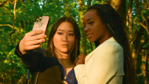 In a sunlit forest, two individuals pose for an elegant selfie, capturing their formal attire's sleek lines—perfect for sharing and boosting their Instagram analytics.