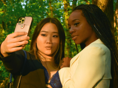 In a sunlit forest, two individuals pose for an elegant selfie, capturing their formal attire's sleek lines—perfect for sharing and boosting their Instagram analytics.