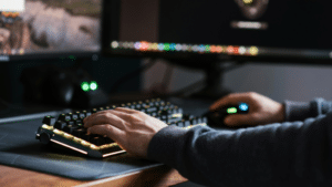 A person is immersed in their work at a computer desk, using a keyboard and mouse while two monitors display dynamic content. Spatial audio enhances the experience, creating an enveloping soundscape that complements the visual engagement.