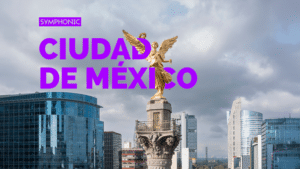 The image shows Mexico City with the Angel of Independence statue in the foreground, surrounded by modern skyscrapers under a cloudy sky.