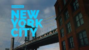 A view of a bridge in New York City with large blue text overlay reading "New York City" and a nearby brick building.