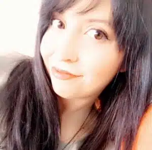 Close-up of a person with long dark hair, smiling softly at the camera. The background is softly lit.