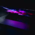 A partially open laptop with a colorful, abstract display screen, emitting a purple glow in a dark environment, captures the essence of innovation. The scene resembles the dynamic visual experience that SplitShare aims to deliver through seamless content sharing.