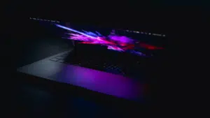 A partially open laptop with a colorful, abstract display screen, emitting a purple glow in a dark environment, captures the essence of innovation. The scene resembles the dynamic visual experience that SplitShare aims to deliver through seamless content sharing.