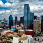 Aerial view of a modern city skyline with tall skyscrapers and cloudy sky above.