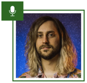 Person with shoulder-length hair in a floral shirt, against a blue background, inside a green-bordered frame with a microphone icon in the corner.