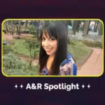 A person with long dark hair smiles outdoors in a garden, embodying the warmth and connection of our community. The text "A&R Spotlight" graces the bottom of the image, inviting you to meet our team.