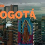 Skyline of Bogotá featuring a vibrant mural of the Virgin Mary on a building, set against a backdrop of modern high-rises and cloudy skies.