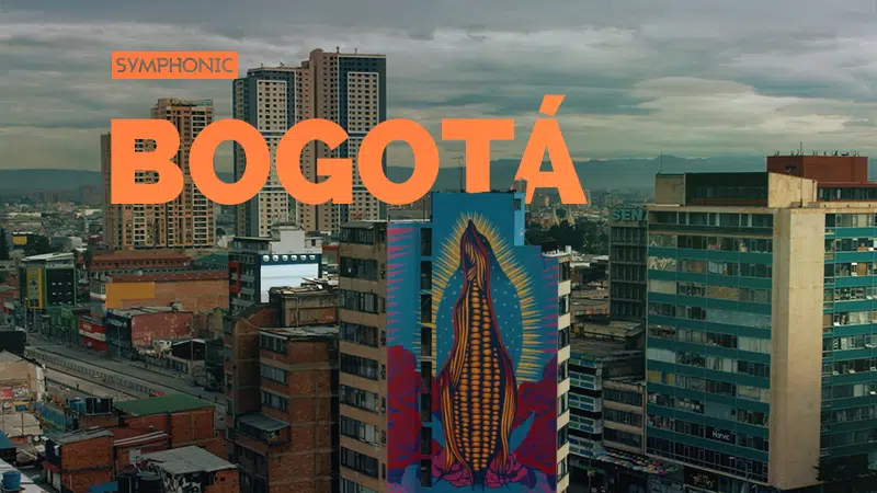 Skyline of Bogotá featuring a vibrant mural of the Virgin Mary on a building, set against a backdrop of modern high-rises and cloudy skies.