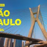 Cabled bridge in São Paulo, Brazil, weaves a story against the sprawling cityscape under a clear blue sky; bold yellow text reads "SYMPHONIC SÃO PAULO BRASIL.