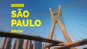 Cabled bridge in São Paulo, Brazil, weaves a story against the sprawling cityscape under a clear blue sky; bold yellow text reads "SYMPHONIC SÃO PAULO BRASIL.