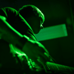 A person playing guitar on stage with green lighting illuminating the scene.