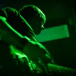 A person playing guitar on stage with green lighting illuminating the scene.