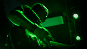 A person playing guitar on stage with green lighting illuminating the scene.