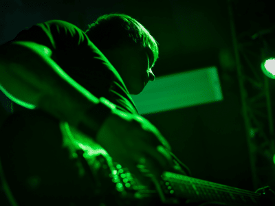 A person playing guitar on stage with green lighting illuminating the scene.