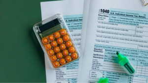 A calculator and two highlighters rest on completed U.S. 1040 individual income tax forms, capturing the challenges of filing taxes as an independent musician, all set atop a green surface.