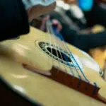 Close-up of a person playing a guitar, as if preparing for a musical conference. The focus is on the strings and body of the instrument, with blurred background elements enhancing the sense of intimate practice before a big performance.