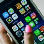 A hand with pink nail polish holds a smartphone displaying various app icons such as settings, photos, Instagram, and WhatsApp on the home screen.