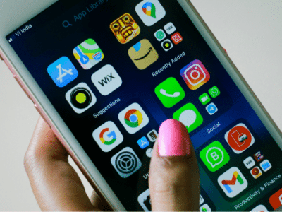 A hand with pink nail polish holds a smartphone displaying various app icons such as settings, photos, Instagram, and WhatsApp on the home screen.