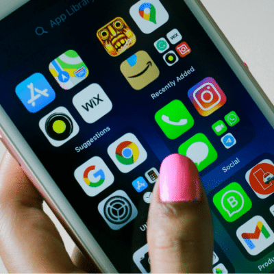 A hand with pink nail polish holds a smartphone displaying various app icons such as settings, photos, Instagram, and WhatsApp on the home screen.