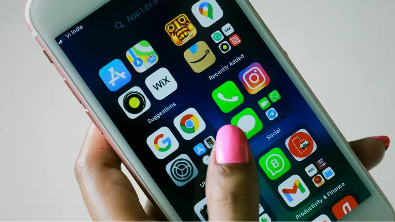 A hand with pink nail polish holds a smartphone displaying various app icons such as settings, photos, Instagram, and WhatsApp on the home screen.