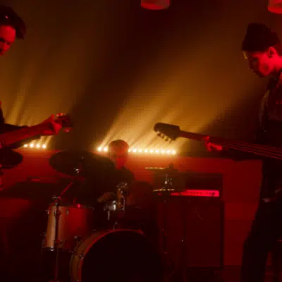 Band performing with electric guitars and drums under warm, dramatic lighting.