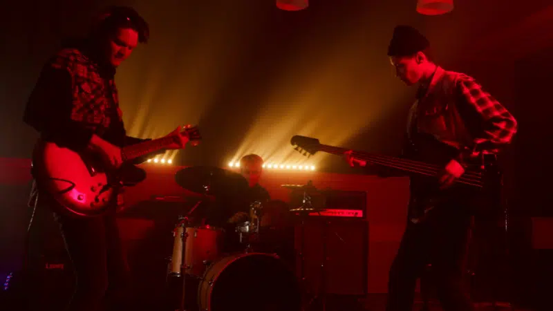 Band performing with electric guitars and drums under warm, dramatic lighting.