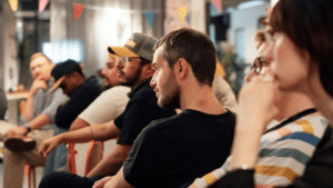 Top Conferences in Asia Every Musician Should Know About A group of people sit in a row at an indoor event. They appear attentive and engaged. Colorful banners hang above them.
