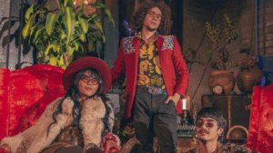 Three people dressed in eclectic, retro-style clothing pose in a vintage room with red furniture and plants.