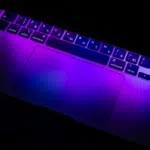 The laptop keyboard and trackpad, illuminated by purple and blue light, create a symphonic visual with Russian Cyrillic characters dancing elegantly across the keys.