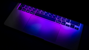 The laptop keyboard and trackpad, illuminated by purple and blue light, create a symphonic visual with Russian Cyrillic characters dancing elegantly across the keys.