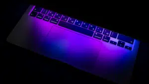 The laptop keyboard and trackpad, illuminated by purple and blue light, create a symphonic visual with Russian Cyrillic characters dancing elegantly across the keys.