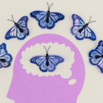 A purple silhouette of a human head with a butterfly inside its brain area, symbolizing mental health, is surrounded by five blue butterflies arranged in an arc above it.