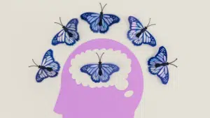 A purple silhouette of a human head with a butterfly inside its brain area, symbolizing mental health, is surrounded by five blue butterflies arranged in an arc above it.
