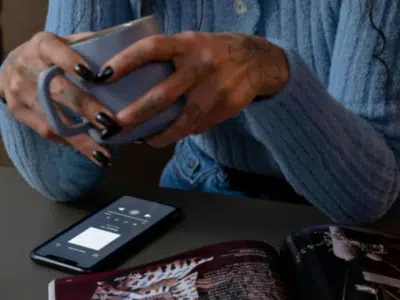 A person is holding a mug, sitting at a table with a smartphone displaying a music app, an open magazine, and their earphones ready for the next masterclass.